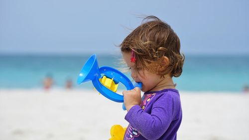 Cute girl holding toy while playing at beach against sky