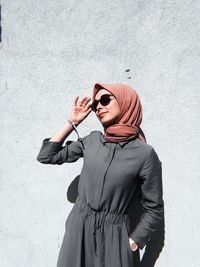 Young woman looking away while wearing sunglasses standing against wall