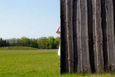 Cropped image of woman hiding behind fence on field