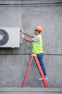 Side view of technician repairing air conditioner