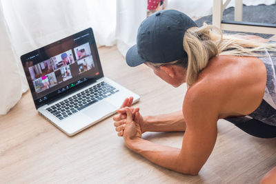 From above back view of fit female athlete in sportswear watching video online on laptop before home workout