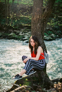 Young woman sitting on tree by river
