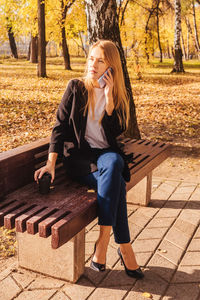 Full length of woman drinking coffee while talking over phone on bench