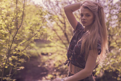 Portrait of young woman standing against trees at park