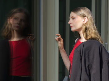 Portrait of young woman standing against window