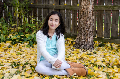 Portrait of smiling girl sitting on leaves covered field during autumn