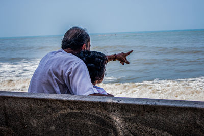 Grandfather with granddaughter looking at sea while sitting on bench