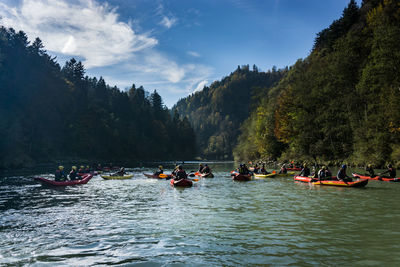 People on river by trees against sky