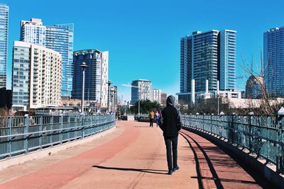 Rear view of man walking in city against blue sky