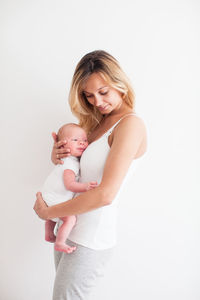 Mother carrying baby while standing against white background