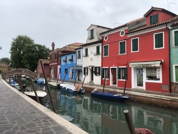 Boats moored in canal by buildings against sky