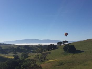 Hot air balloon flying over landscape against clear blue sky