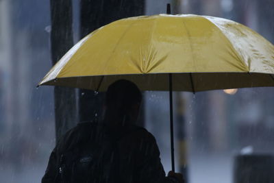 Rear view of man with umbrella standing in rain during monsoon