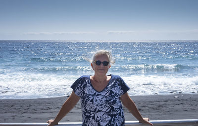 Portrait of young man wearing sunglasses on beach against sky