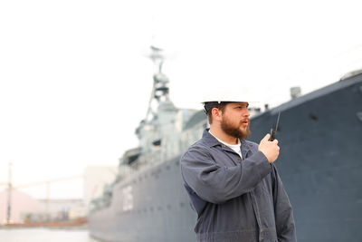 Sailor using walkie talkie while standing against ship