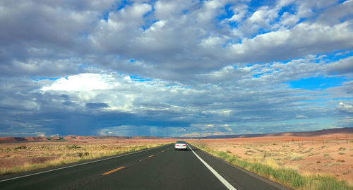 Road passing through landscape against cloudy sky