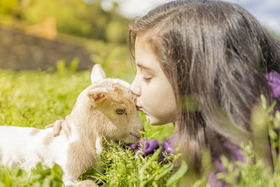 Close-up of cute girl kissing kid goat on grassy land