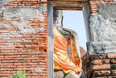 Low angle view of buddha statue behind abandoned wall