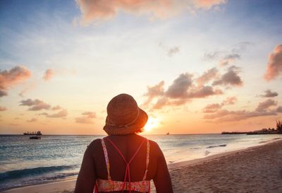 Rear view of woman standing at beach during sunset