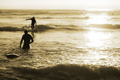 Silhouette people in sea against sky during sunset