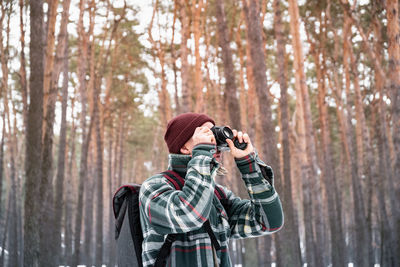 Man photographing while standing in forest during winter