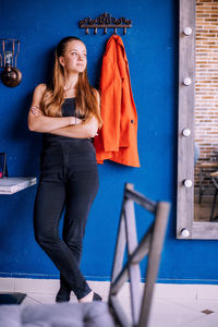A young woman on the background of a blue wall. a red jacket hangs nearby. a glance to the side.