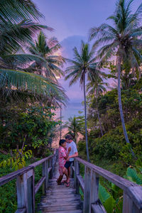 Girl and woman standing on railing by palm trees against sky