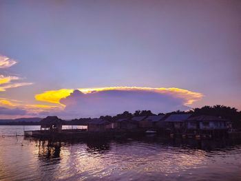 Houses by lake against sky during sunset