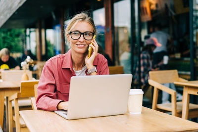 Young attractive caucasian woman sitting in a cafe works on a laptop and speaks on the phone.