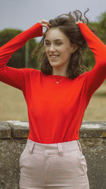 Smiling young woman standing against red wall