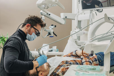 Young dentist examining patient's teeth with equipment in clinic