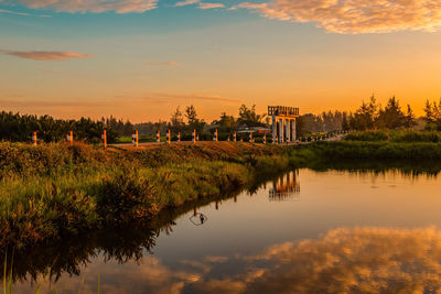 Scenic view of lake by building against sky during sunset