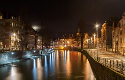 Illuminated bridge over canal amidst buildings in city at night