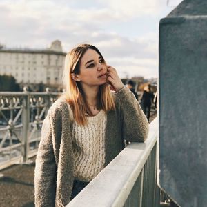 Close-up of young woman against railing and cityscape against sky