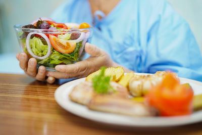 Midsection of man holding fruit salad in plate on table