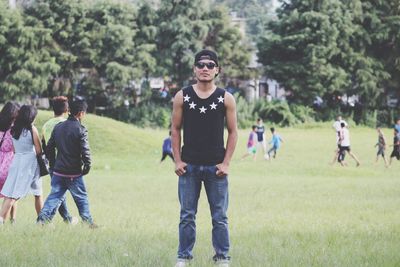 Portrait of young man wearing sunglasses standing on grassy land in park