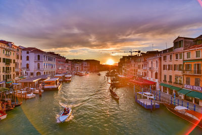 Boats in canal amidst buildings against sky during sunset