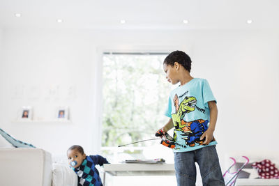 Boy holding remote of model airplane while looking at brother in living room