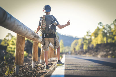 Rear view of boy with backpack standing on road against clear sky
