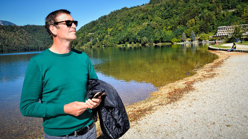 Young man wearing sunglasses standing by lake against trees