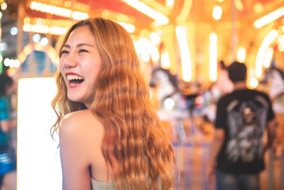 Smiling young woman standing against carousel