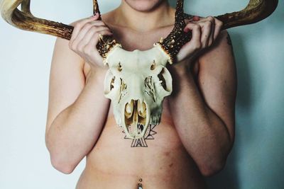 Midsection of shirtless woman holding skull against wall