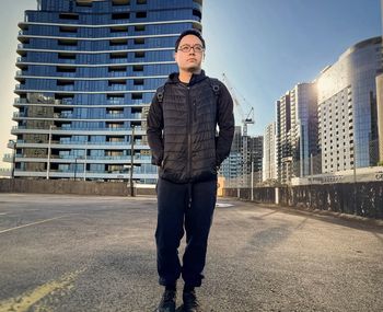 Young asian man standing against buildings, construction crane and sky.