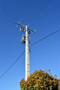 Low angle view of electricity pylon by tree against clear sky