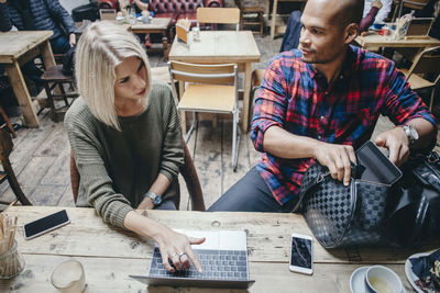 Woman using laptop while discussing with man in coffee shop