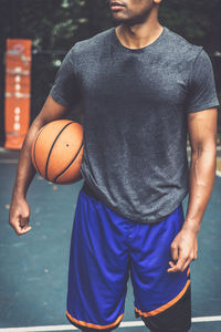 Midsection of man holding basketball ball on court