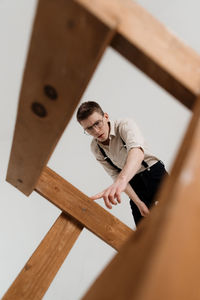 Low angle view of young man with wooden ladder against white background
