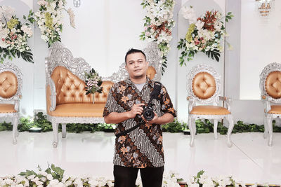 Portrait of young man in front of wedding chair smiling and holding camera