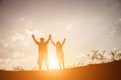 Friends with arms raised standing against sky during sunset