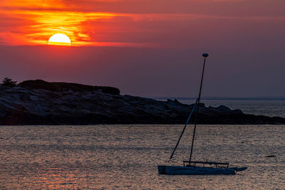 Boat silhouetted as the sun sets beyond clouds over the ocean's harbor